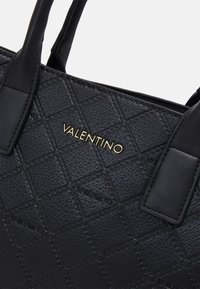 Czarna skórzana torba typu tote z pikowanym wzorem i złotymi detalami z logo. Posiada usztywnioną konstrukcję i podwójne uchwyty. Teksturowana powierzchnia dodaje głębi.