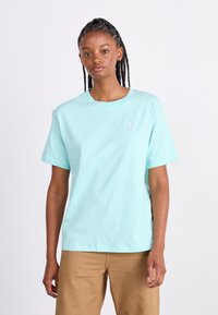 Mintgrøn bomulds T-shirt med korte ærmer og rund hals, med et lille hvidt logo på brystet. Bæres med khaki bukser.