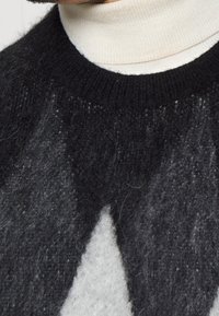 Svart och grå texturerad tröja med ett kontrasterande vitt triangelnmönster, som har en ribbad halsringning och mjukt, fuzzy ullmaterial.