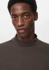 Camiseta de manga larga de alto cuello en un tono marrón oscuro, hecha de una tela suave, con costuras mínimas y una silueta ajustada. Sin patrones ni acentos visibles.