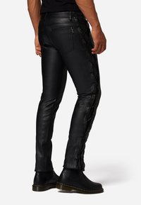 Schwarze Lederhosen mit schmaler Passform, filigranen gewebten Details an den Seiten und zwei Gesäßtaschen, kombiniert mit schwarzen Knöchelstiefeln.