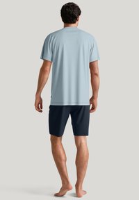 Lichtblauw kortemouwenshirt met een rechte zoom, gecombineerd met marineblauwe shorts. De stof lijkt licht en glad te zijn. Geen zichtbare patronen.