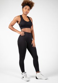 Černý sportovní top s krátkým střihem a legíny s vysokým pasem, které mají hladkou strukturu. Bílé sportovní boty s detailními akcenty na bocích.