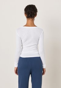 Valge pika varrukaga särk ümarate kaelustega, istuva lõikega ja pehme tekstuuriga, kombineeritud tumesiniste, lõdva lõikega pükstega. Märkimisväärseid detaile ei ole.