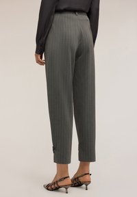 Harmaat ruudulliset housut, joissa on muotoon ommeltu malli, lyhyt pituus ja nappikoristeet hihaosuissa, yhdistettynä nauhakahvaisiin korkokenkiin.