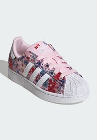 Adidase Superstar tossud on roosades, punastes ja sinistes toonides lillemustriga, valge kolme triibu disaini ja kummist kestaga varbaga.