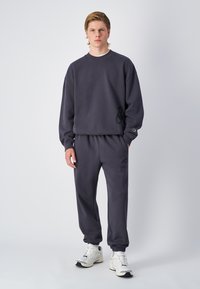 Sweatshirt gris foncé et joggeurs assortis en tissu doux. Dotés de poignets côtelés, d'une taille élastique et d'accents de logo discrets.
