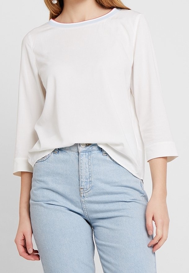 Top bianco a maniche lunghe con colletto rotondo e rifiniture a contrasto, abbinato a jeans in denim chiaro a vita alta.