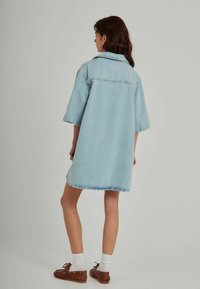 Ljusblå denim oversized skjortklänning med korta ärmar, krage och fransade fållar, i kombination med bruna skor och vita strumpor.