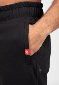 Zwarte joggers gemaakt van zachte stof, met een elastische tailleband, zijzak en een klein rood logotag op de zak.