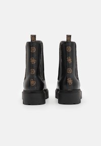 Bottes noire en cuir à la cheville avec une semelle épaisse et des panneaux décoratifs à motifs. Équipées d'une languette à l'arrière pour un enfilage facile.