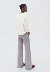 Bela pletena jopica z ohlapnim krojem, v kombinaciji s svetlo sivo širokima hlačami, ki imajo subtilno teksturo in stranske žepe.