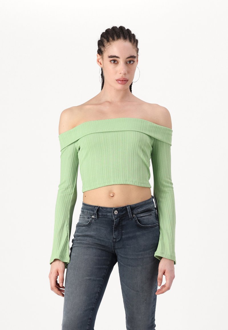 Zeleni rebrasti top bez naramenica s dugim rukavima, prilagođenog kroja i skraćenog dizajna, uparen s tamnosivim slim-fit trapericama.