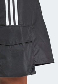 Black sports jacket featuring three white horizontal stripes, smooth fabric, a front pocket, and a slight side slit at the hem.