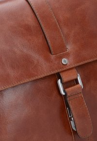 Bruine leren tas met een gladde textuur, voorzien van een zilveren gesp en een drukknopsluiting. Het ontwerp bevat stiksels langs de randen.