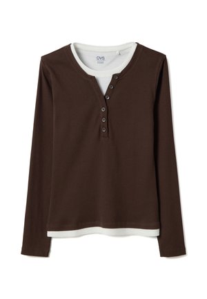 Camiseta henley marrón de manga larga superpuesta sobre una camiseta blanca de cuello redondo, con botones visibles en la tapeta de la camisa marrón.