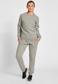 Lichtgrijze katoenen sweatshirt en bijpassende joggers, met ribgebreide mouwen, een relaxte pasvorm en zijzakken. Gekozen met zwarte sportschoenen.