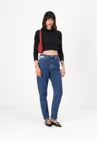 Svart kortermet topp med lange ermer, blå høy midje jeans og svarte spisse leiligheter. Rød skulderveske. Glatt tekstur, uformell design.