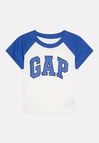 Hvit t-skjorte med blå raglanermer og en "GAP" logo i fete blå bokstaver på forsiden. Laget av bomull, med rund halsdesign.