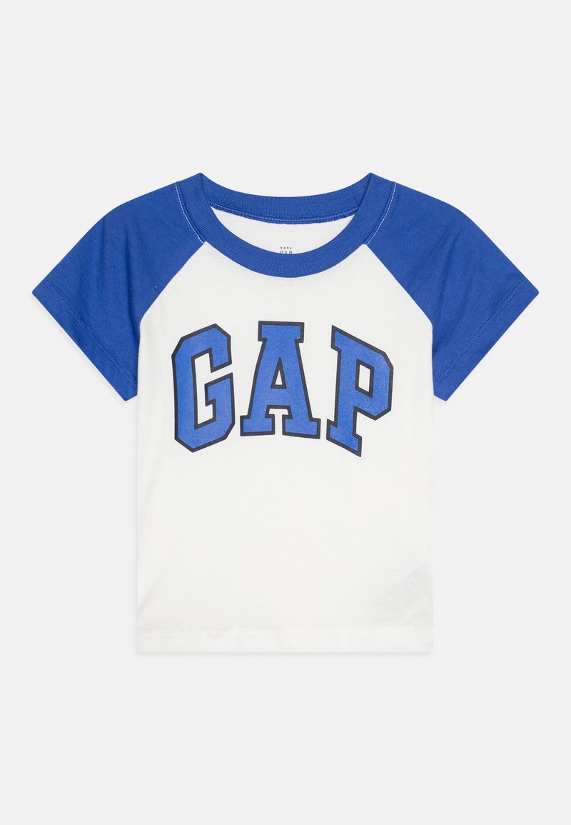 Hvit t-skjorte med blå raglanermer og en "GAP" logo i fete blå bokstaver på forsiden. Laget av bomull, med rund halsdesign.