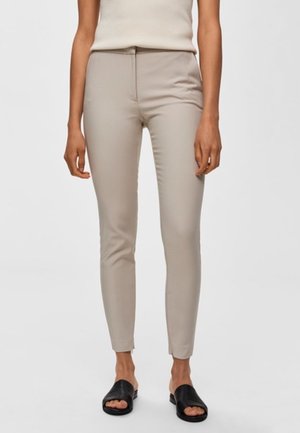Pantalones beige ajustados hechos de una tela suave, con una cintura de altura media y una silueta ajustada, combinados con sandalias negras de tipo slide.