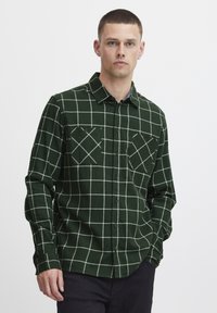 Cămașă verde cu carouri, din flanel, cu model de grilă albă, guler cu nasturi, două buzunare pe piept și mâneci lungi.