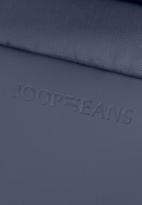 Námořnický modrý materiál má jemnou ribbovanou strukturu, s vytlačeným logem "JOOP JEANS" v dolní části. Design je jednoduchý a moderní.
