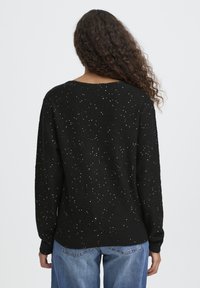Black sweater featuring a relaxed fit, round neck, and long sleeves, adorned with scattered white sequins for texture and visual interest.