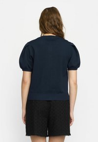Mørkeblå strikket sweater med pufærmer og ribbet kant, parret med sorte shorts med et dekorativt hulmønster.