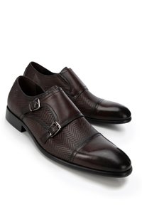 Zapatos de cuero marrón oscuro con un patrón de espiga, doble hebilla y una punta redondeada elegante. El tacón bajo tipo bloque aporta estabilidad.