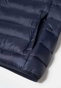 Laivasto sininen puhvitakki, jossa on tilkkupinta, varustettuna vetoketjullisella taskulla ja pehmeällä vuorilla. Sujuva, eristetty kangas lämmittämään.