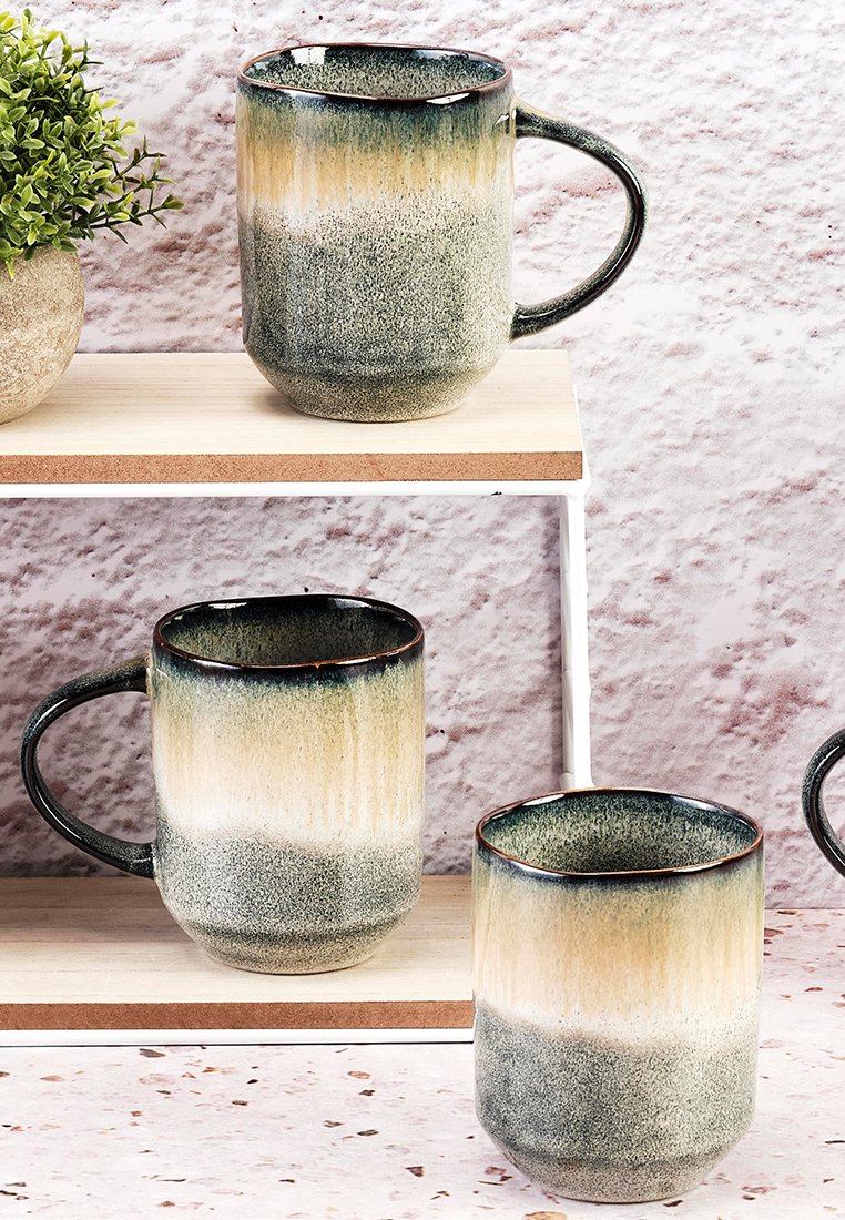Trzy ceramiczne kubki o teksturowanym, gradientowym wykończeniu przechodzącym od ciemnej zieleni do jasnego beżu, z solidnym uchwytem i okrągłym kształtem.