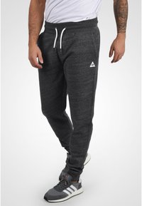 Pantalones de chándal gris oscuro hechos de un tejido suave y texturizado. Cuentan con una cintura elástica con cordones y bolsillos laterales. Pequeño logotipo en la cadera.