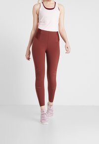 Leggings bordeaux a vita alta e tasche laterali, con dettagli a pois e una consistenza liscia e elastica. Abbinati a un top leggero senza maniche.