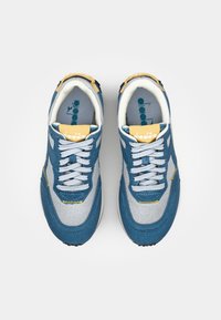 Blue and gray sneakers with a suede and mesh upper, white laces, yellow accents, and a cushioned sole, featuring a logo on the tongue.