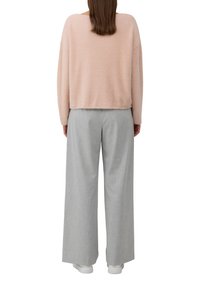 Pull rose clair en peluche avec une coupe ample, associé à un pantalon gris à jambes larges et des baskets blanches. La tenue est décontractée et confortable.