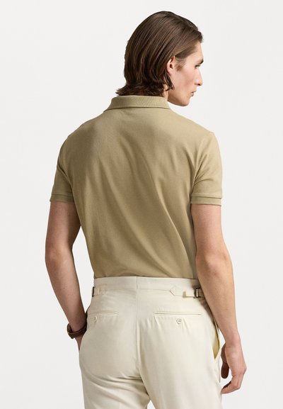 Beige polo krekls ar mīkstu tekstūru, īsām piedurknēm un klasisku apkakli, kombinēts ar gaišas krāsas elegantiem biksēm ar jostu.