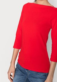 Rotes Langarmshirt mit weiter Bootskragenlinie, aus glattem Baumwollstoff gefertigt. Verfügt über eine taillierte Silhouette und mittellange Ärmel.
