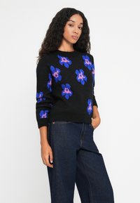 Zwarte trui met blauwe en roze bloemmotieven, gestructureerde brei, ronde halslijn en geribbelde manchetten, gecombineerd met donkere denim wijde broek.