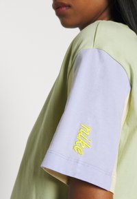 Tričko Nike s designem v levandulové a světle zelené barvě bloky, s žlutou výšivkou na rukávu a měkkou, texturovanou tkaninou.
