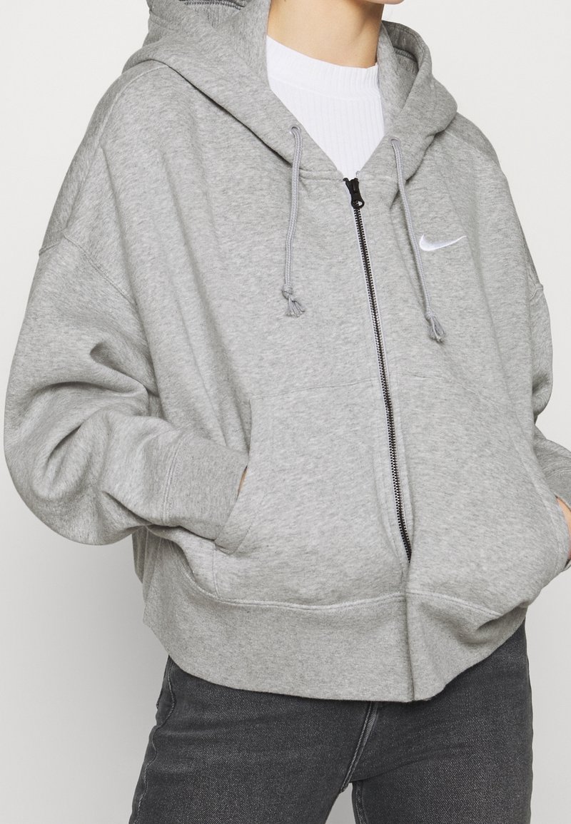 Sweat à capuche zippé gris clair en tissu doux. Comprend une poche kangourou, une capuche avec cordon de réglage et un petit logo sur la poitrine.