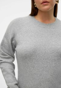 Pull tricoté gris avec un col rond et des manches raglan. Texture moyenne avec une finition douce. Design uni sans motifs ni accents.