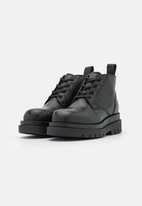 Stivali alla caviglia in pelle nera con punta rotonda, design con lacci, toppe rinforzate e suole in gomma testurizzata. Presentano una linguetta sul retro.