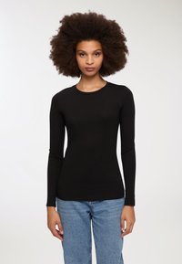 Czarna, dopasowana koszula z długim rękawem i okrągłym dekoltem. Gładki materiał w połączeniu z jasnoniebieskimi jeansami o wysokim stanie. Prosty, minimalistyczny design.