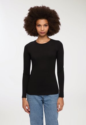 Maglietta nera a maniche lunghe aderente con scollo rotondo. Tessuto morbido abbinato a jeans a vita alta di colore blu chiaro. Design semplice e minimalista.