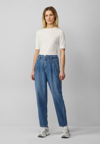 Top corto blanco ligero de manga corta combinado con jeans azul de cintura alta y corte relajado, que cuentan con una cinturilla texturizada y bolsillos inclinados.