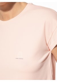 Lichtroze T-shirt van katoen, met opgerolde korte mouwen en een kleine witte afbeelding van een beanie met daaronder de tekst "SHORT STORIES".