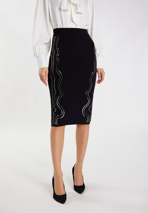 Zwarte kokerrok van textuurstof, met golvende zilveren versieringen langs de zijkanten. Gestyled met een witte blouse en zwarte hakken.