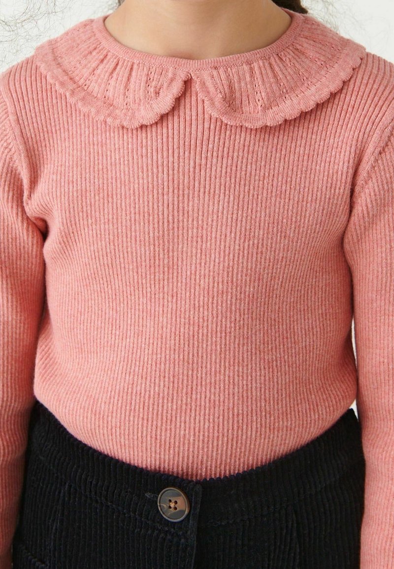 Enfant portant un pull rose côtelé avec un col festonné et un pantalon en velours côtelé noir avec une taille boutonnée.