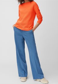 Pull orange vif à manches longues associé à un pantalon large bleu clair. Le pantalon possède des poches avant et est fabriqué dans un tissu doux ressemblant au denim.
